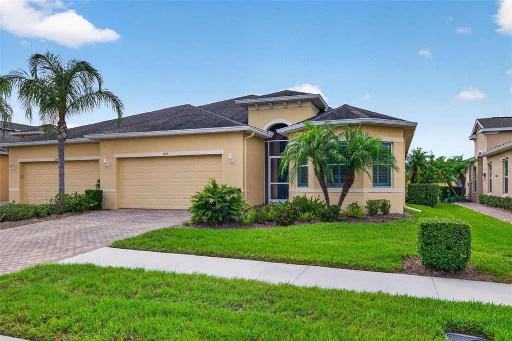 A single-story house with a tan stucco exterior, a two-car garage, and a paved driveway — 712 CHIPPER DRIVE, SUN CITY CENTER, FL