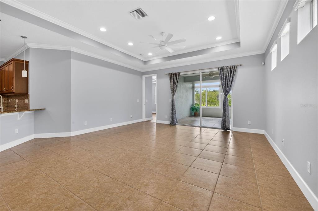 A spacious living room with tile flooring, a tray ceiling, and sliding glass doors — 712 CHIPPER DRIVE, SUN CITY CENTER, FL