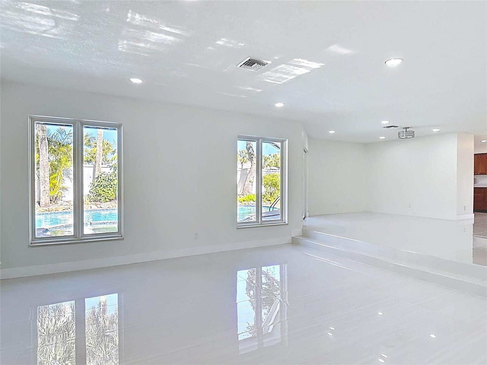 An empty room with white tile floors, recessed lighting, and windows overlooking a swimming pool — 1200 Poitras Drive, Vero Beach FL 32963, VERO BEACH, FL