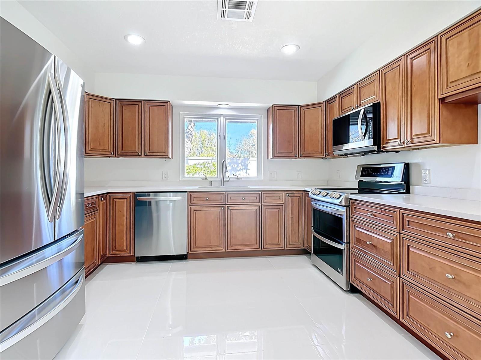 A kitchen features wood cabinets, stainless steel appliances, white countertops, and light-colored tile flooring — 1200 Poitras Drive, Vero Beach FL 32963, VERO BEACH, FL
