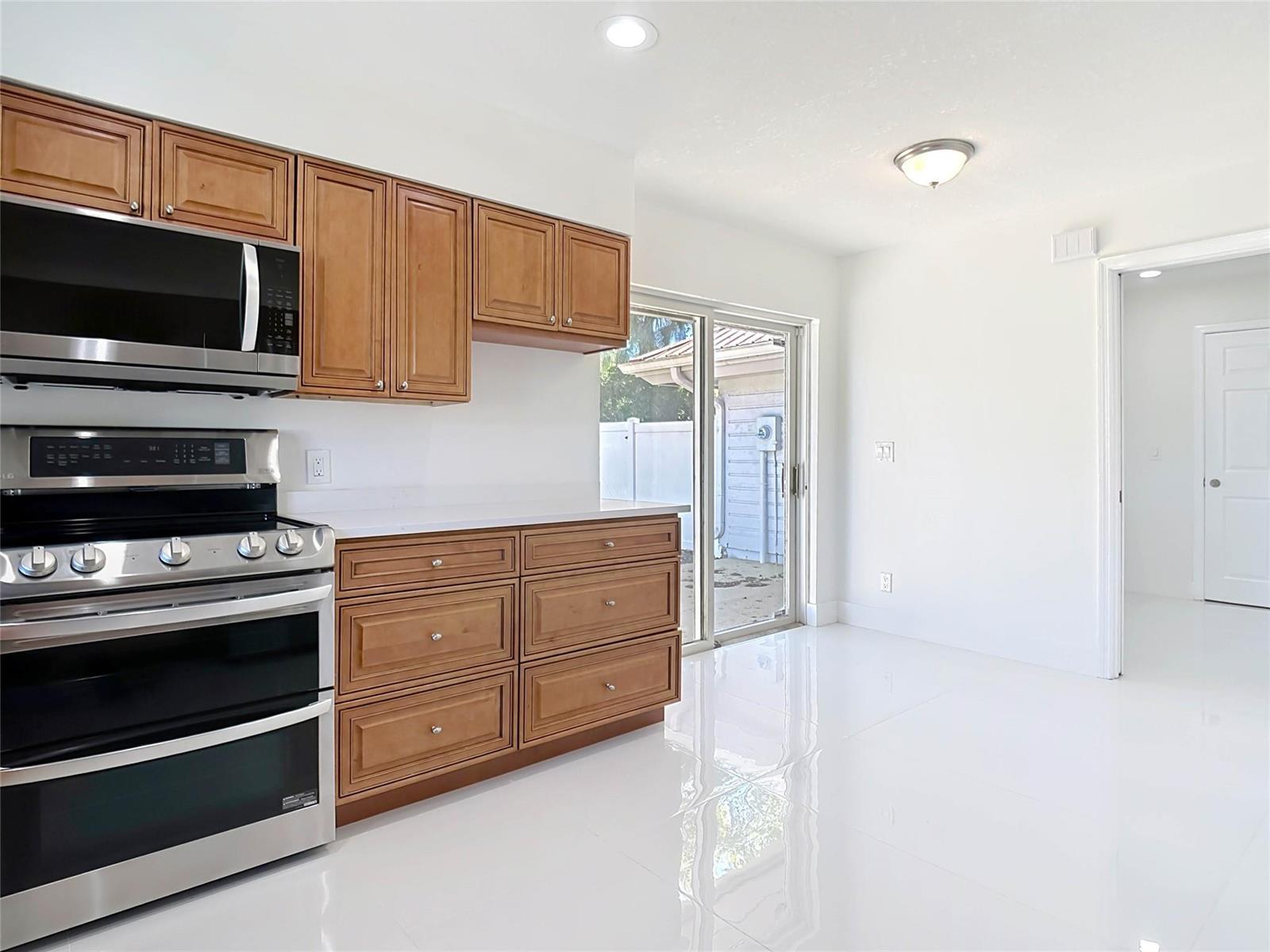 A kitchen with wood cabinets, stainless steel appliances, and white tile flooring leads to a patio — 1200 Poitras Drive, Vero Beach FL 32963, VERO BEACH, FL