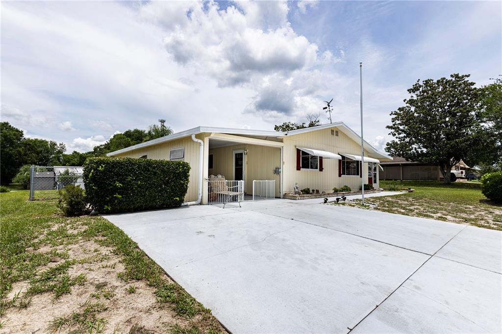 A light-colored single-story house features a concrete driveway, a carport, and a manicured hedge — 9035 SW 102ND PLACE, OCALA, FL