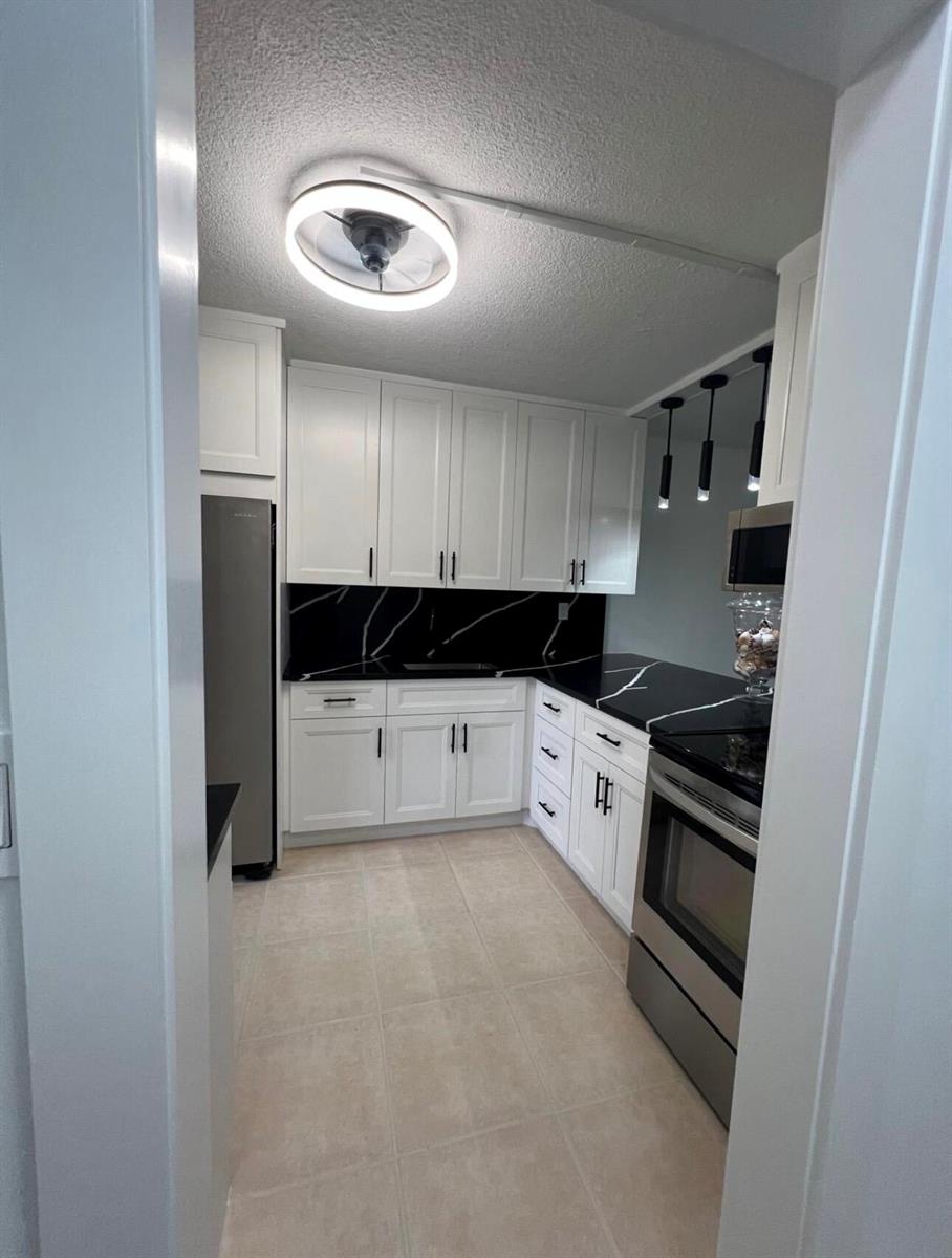 A kitchen with white cabinets, black marble-patterned countertops, stainless steel appliances, and tile flooring — 2615 Garden Drive N # 104, FL 33461, FL