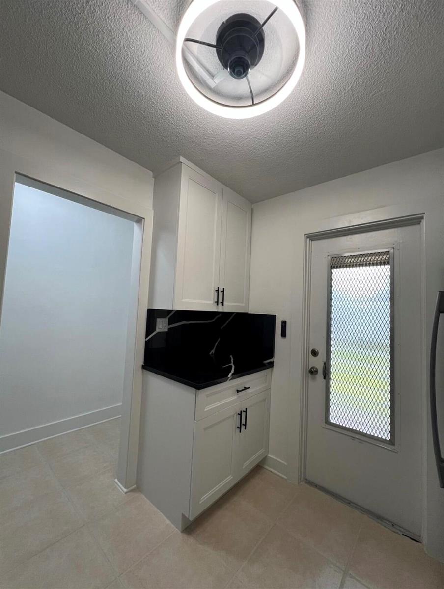 A small kitchen area features white cabinets, a black marble-style backsplash, and a glass-paneled door — 2615 Garden Drive N # 104, FL 33461, FL