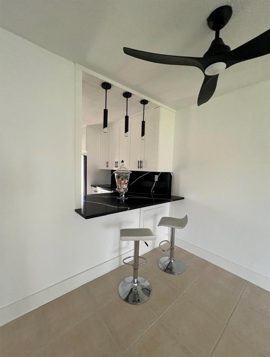 A kitchen pass-through features black marble countertops, white cabinetry, and two modern bar stools — 2615 Garden Drive N # 104, FL 33461, FL
