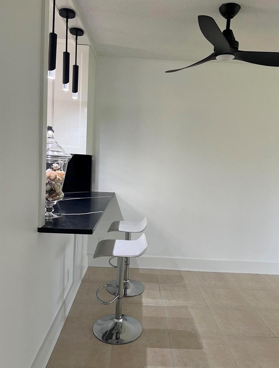 A kitchen breakfast bar with black countertops, pendant lighting, and two stools on tiled floors — 2615 Garden Drive N # 104, FL 33461, FL