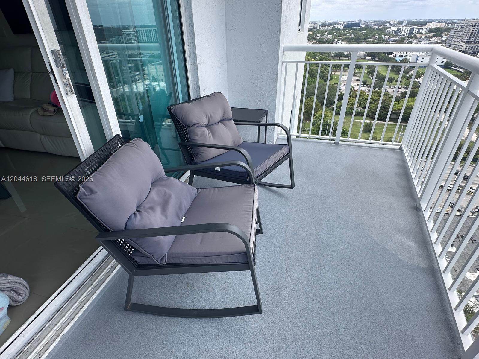 A balcony features two gray rocking chairs with cushions and a small side table — 275 NE 18th St # 1902, Miami FL 33132, MIAMI, FL