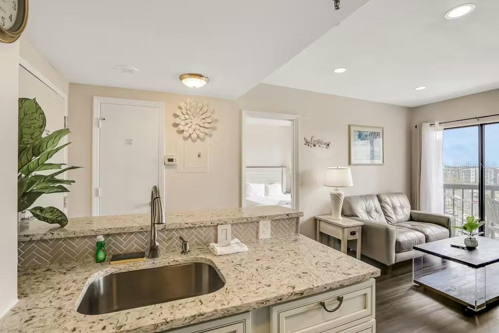 A kitchen island with a granite countertop overlooks a living area with a gray sofa — 6165 CARRIER DRIVE UNIT 3604, ORLANDO, FL