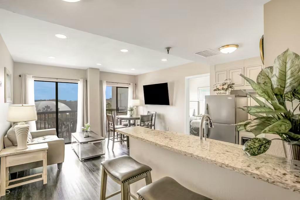An open-concept living and dining area features a kitchen island with granite countertops and stools — 6165 CARRIER DRIVE UNIT 3604, ORLANDO, FL