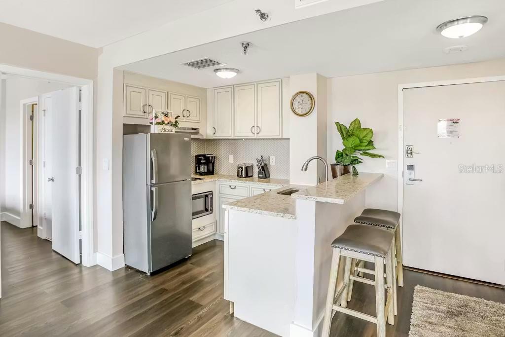 A kitchen features white cabinets, granite countertops, a stainless steel refrigerator, and a breakfast bar — 6165 CARRIER DRIVE UNIT 3604, ORLANDO, FL