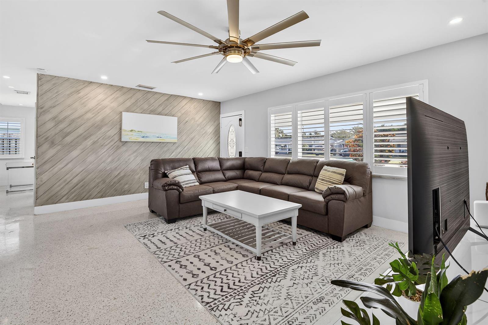 A living room features a brown sectional sofa, a white coffee table, and diagonal wood paneling — 1123 SE 2nd Avenue, Deerfield Beach FL 33441, DEERFIELD BEACH, FL