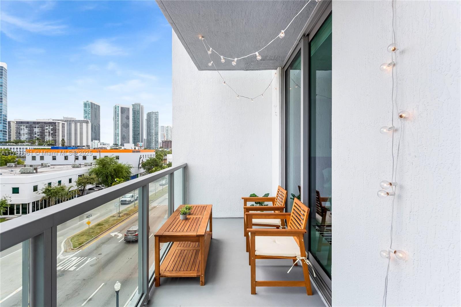 A balcony features two wooden chairs, a matching table, and string lights overlooking a city street — 3900 Biscayne Blvd # 314, Miami FL 33137, MIAMI, FL
