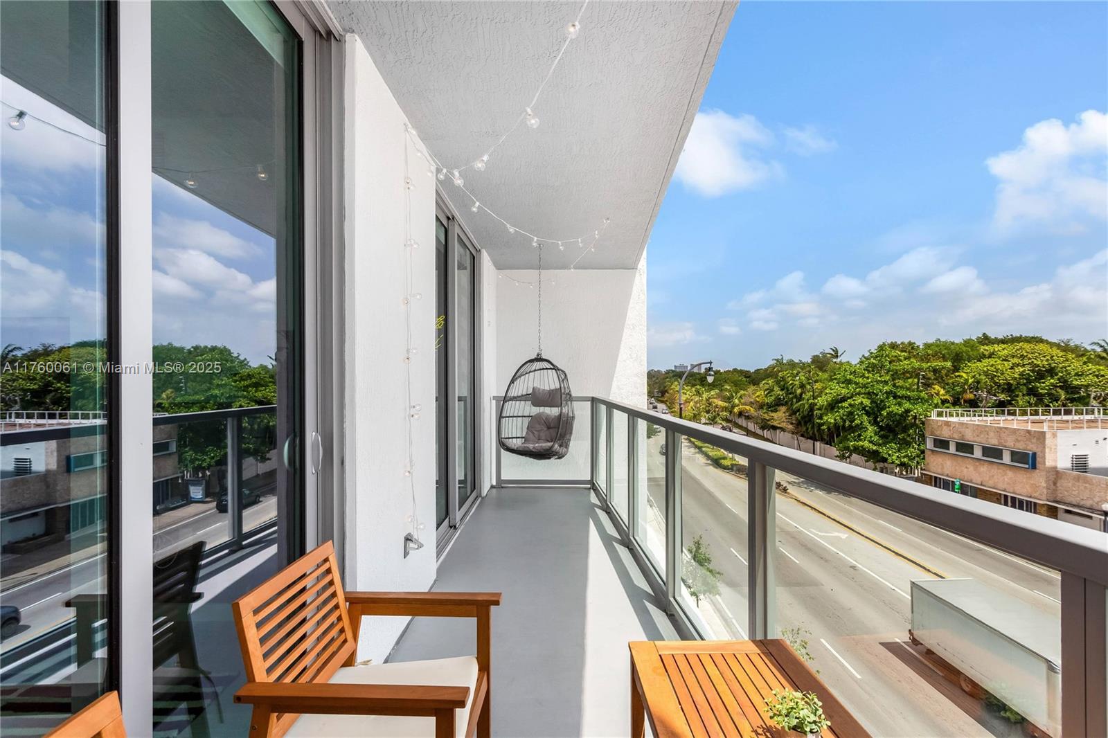 A balcony features a hanging egg chair, wooden furniture, and a glass railing overlooking a street — 3900 Biscayne Blvd # 314, Miami FL 33137, MIAMI, FL
