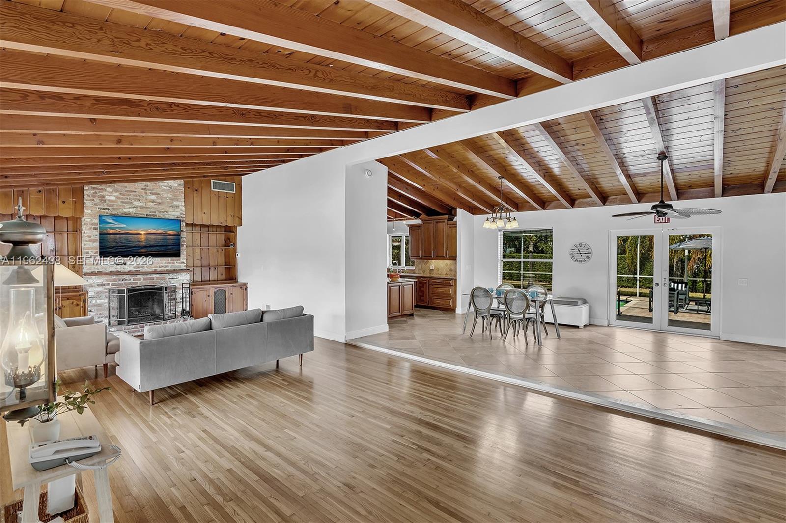 An open-concept living and dining area features wood-beamed ceilings, hardwood floors, and a brick fireplace — 3437 Buchanan St, Hollywood FL 33021, HOLLYWOOD, FL