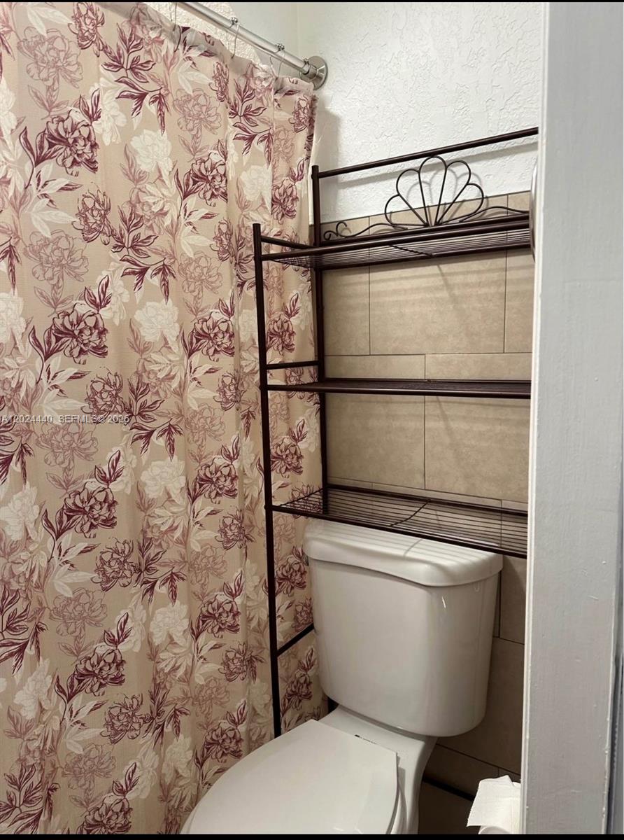 A bathroom features a floral shower curtain, a white toilet, and a metal storage rack — 17649 SW 142nd Ct, Miami FL 33177, MIAMI, FL