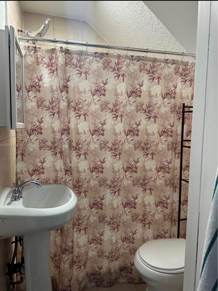 A small bathroom features a pedestal sink, a toilet, and a floral shower curtain — 17649 SW 142nd Ct, Miami FL 33177, MIAMI, FL