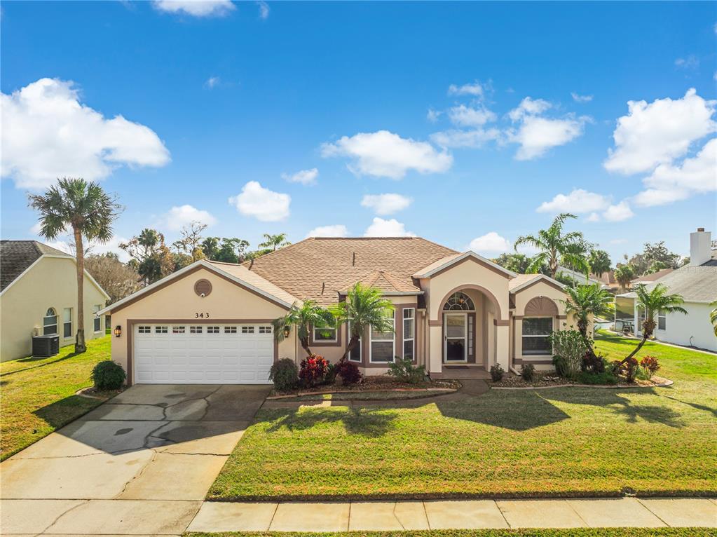 A single-story house with a two-car garage, tan stucco exterior, and palm trees — 343 ALEATHA DRIVE, DAYTONA BEACH, FL