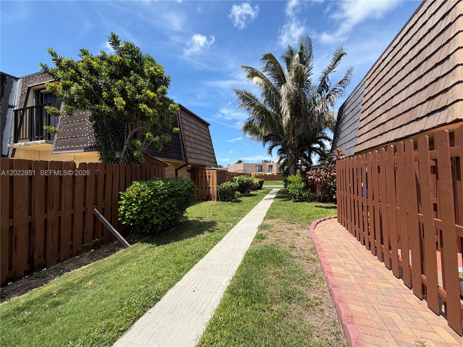 A narrow concrete walkway runs between two brown wooden fences and residential buildings — 964 Springdale Cir, Palm Springs FL 33461, PALM SPRINGS, FL