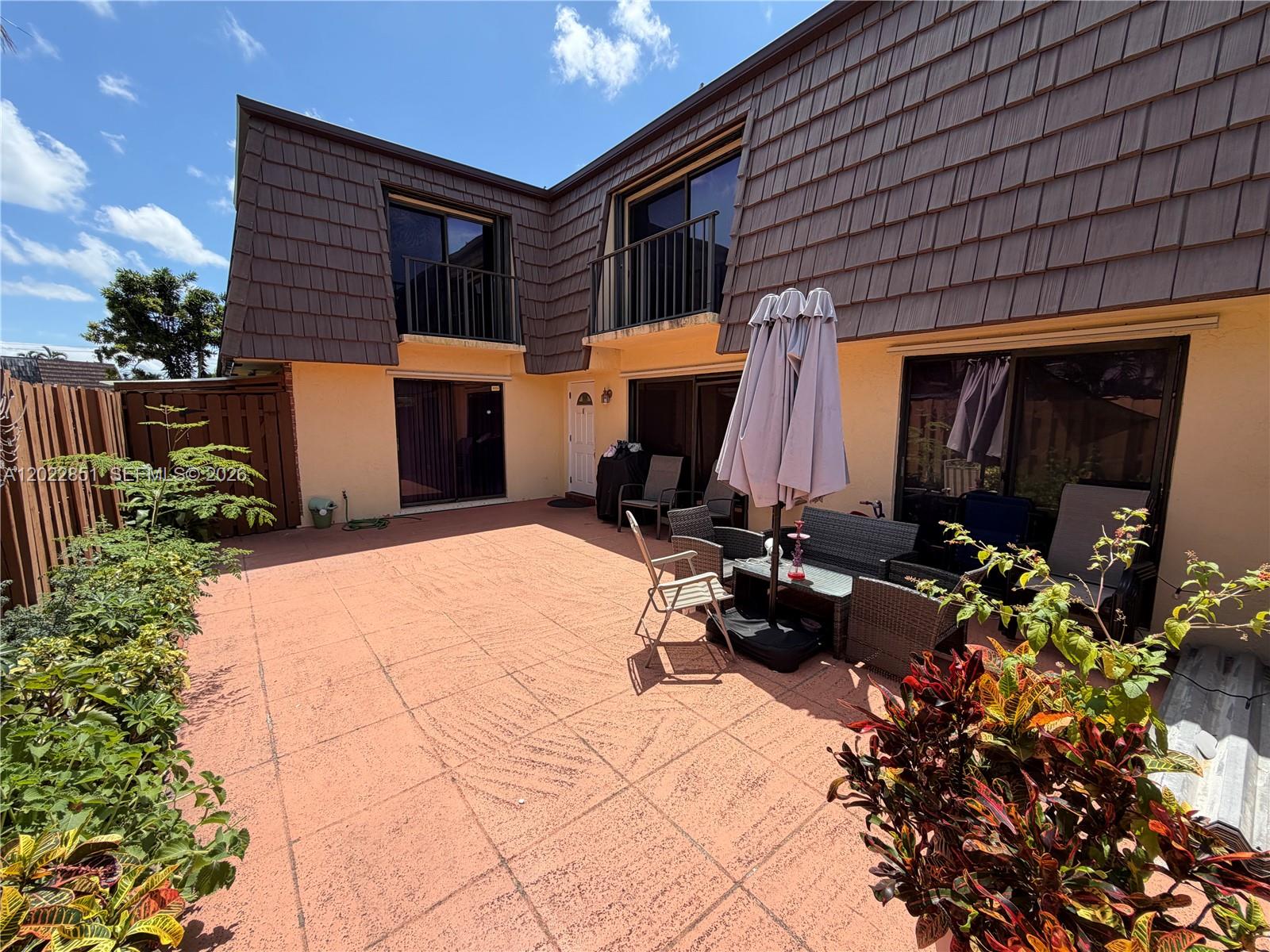 A paved patio area features outdoor furniture, a closed umbrella, and a two-story residential building — 964 Springdale Cir, Palm Springs FL 33461, PALM SPRINGS, FL