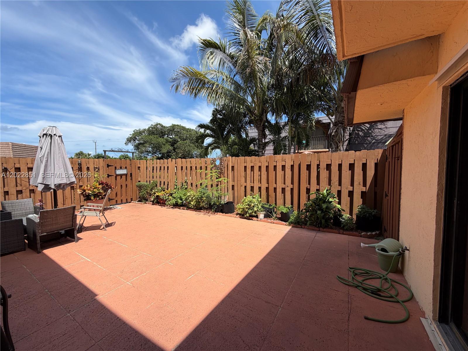 A patio with a wooden fence, potted plants, outdoor furniture, and a green garden hose — 964 Springdale Cir, Palm Springs FL 33461, PALM SPRINGS, FL