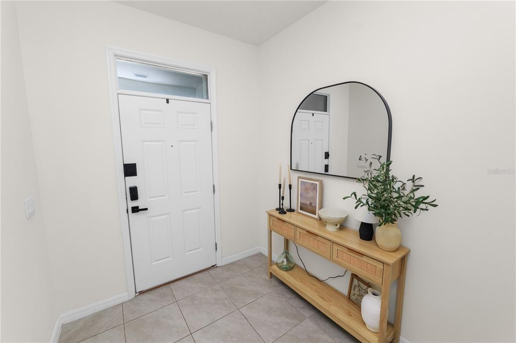 An entryway features a white door, light tile flooring, and a wooden console table with decor — 3830 SUNFLOWER FIELD PLACE, PLANT CITY, FL