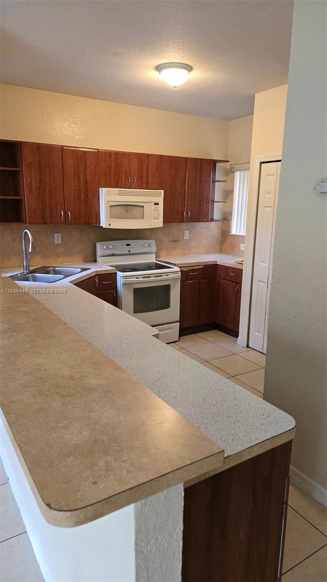A kitchen features wood cabinets, a white stove, a microwave, and a breakfast bar — 671 SW 10th St, Florida City FL 33034, FLORIDA CITY, FL