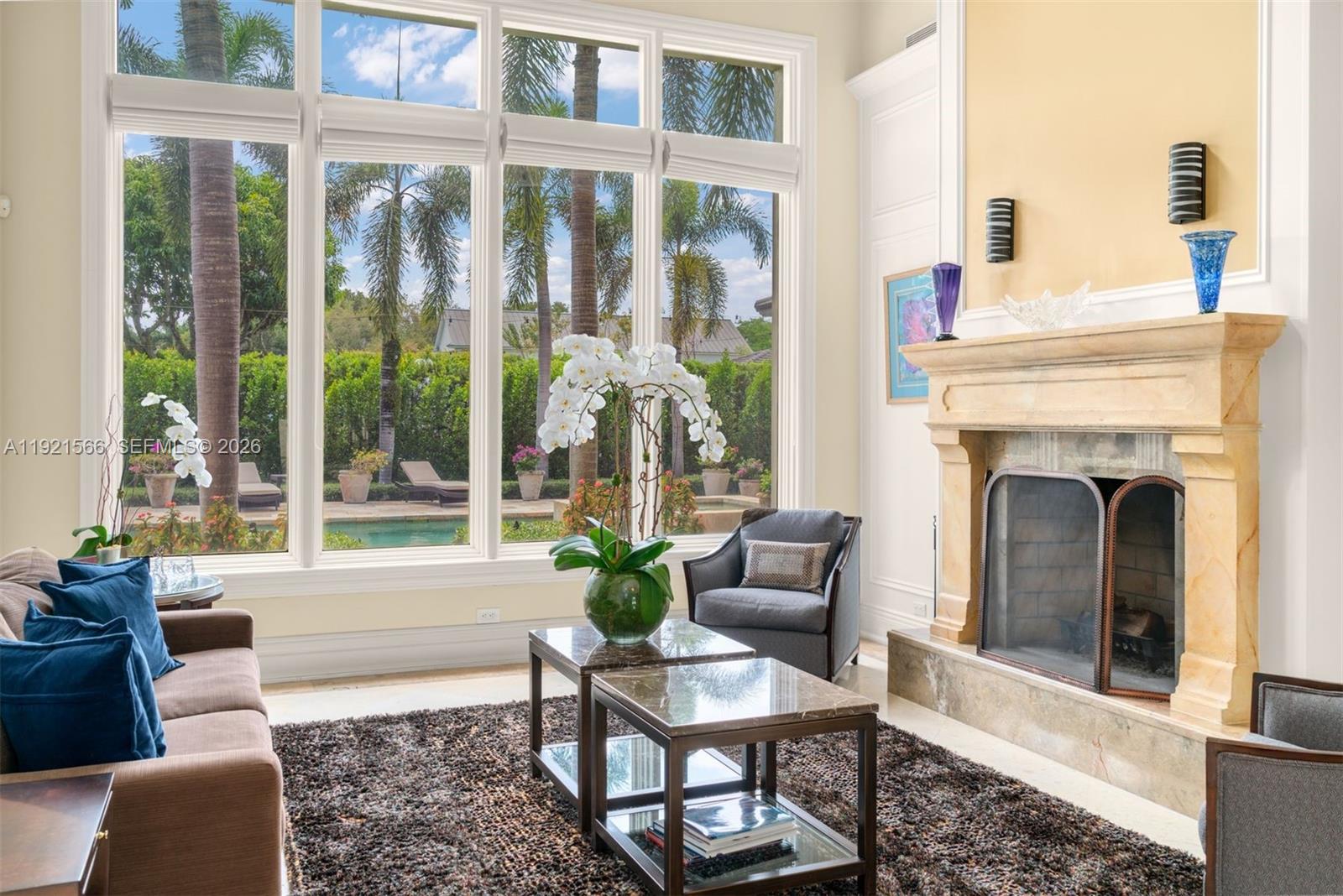 A living room features a stone fireplace, large windows overlooking a pool, and modern furniture — 8010 Ponce De Leon Rd, Miami FL 33143, MIAMI, FL