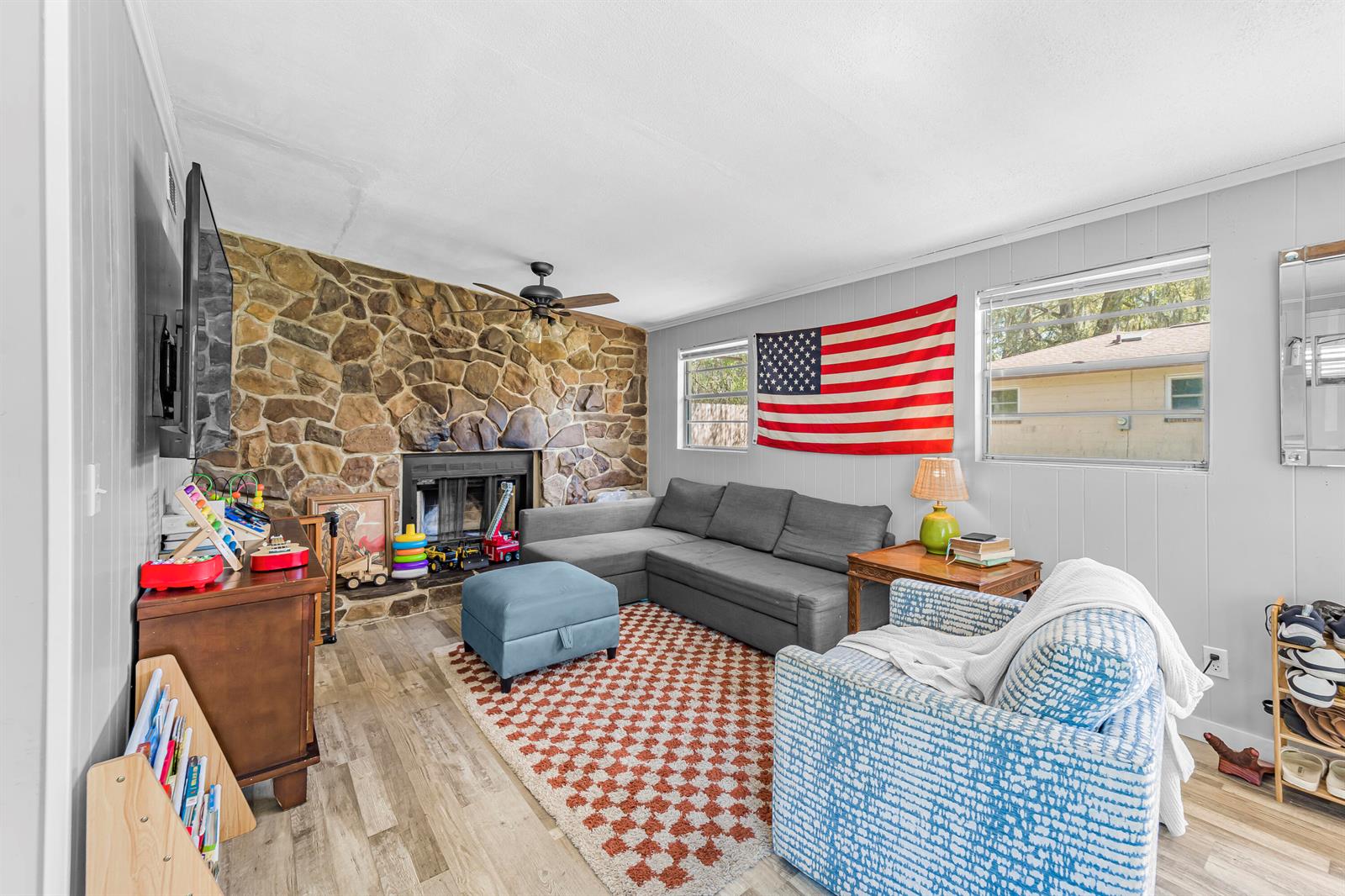 A living room features a stone fireplace, gray sectional sofa, patterned armchair, and wood flooring — 3105 Loretto Road, Jacksonville FL 32223, JACKSONVILLE, FL