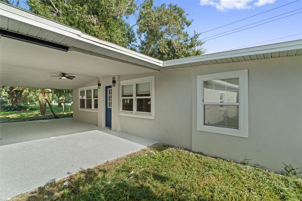 A beige house exterior features a covered carport, a blue door, and several white-framed windows — 929 ADRIAN COURT, LAKELAND, FL