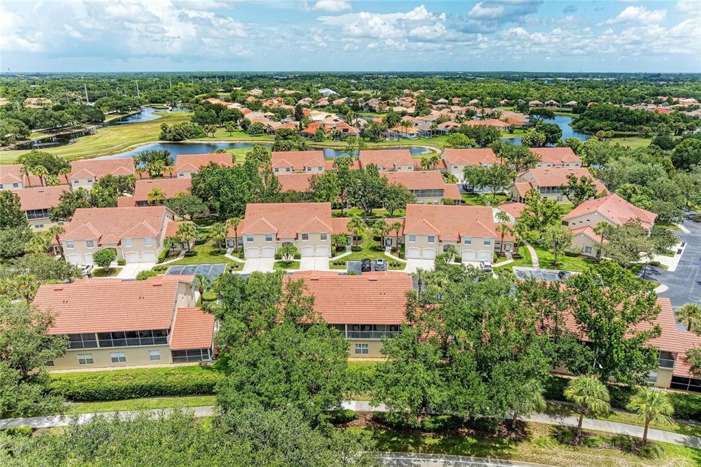 An aerial view shows multiple residential buildings with terracotta roofs surrounded by trees and water — 7126 CEDAR HOLLOW CIRCLE, BRADENTON, FL