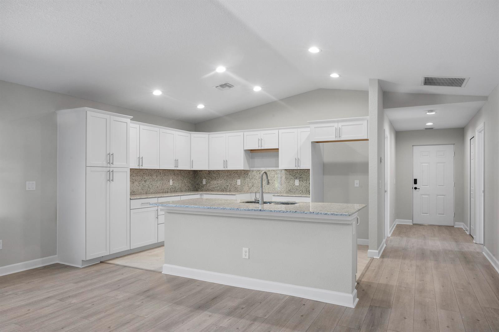A kitchen with white cabinets, granite countertops, a center island, and light wood-look flooring — 41 La Villa Way, Fort Pierce FL 34951, FORT PIERCE, FL