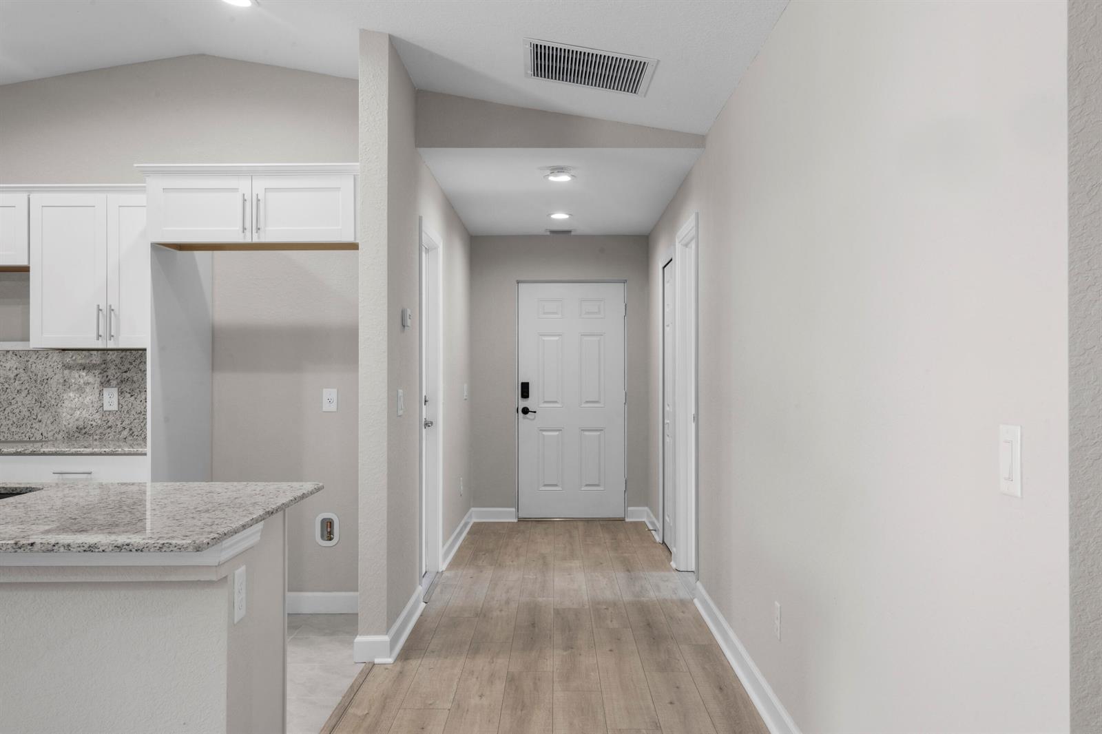 A view of an entryway with light wood flooring, white doors, and a kitchen area — 41 La Villa Way, Fort Pierce FL 34951, FORT PIERCE, FL