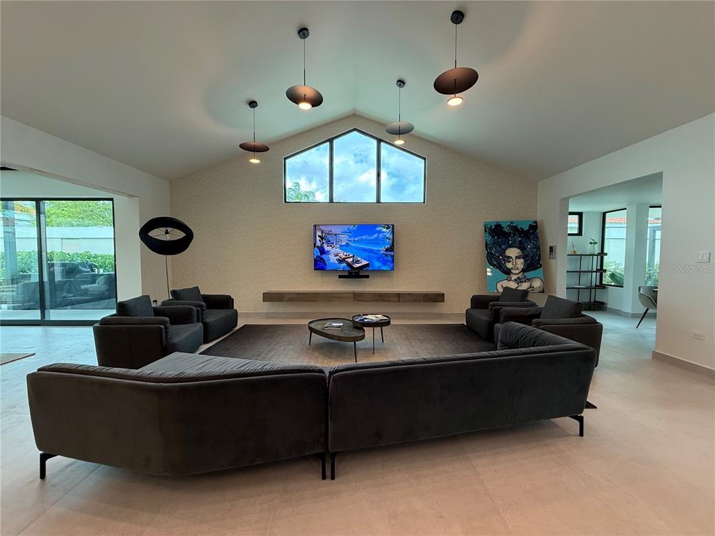 A modern living room features a vaulted ceiling, a wall-mounted television, and dark sectional seating — 241 CAMINO DEL JAGUEY, DORADO, PR