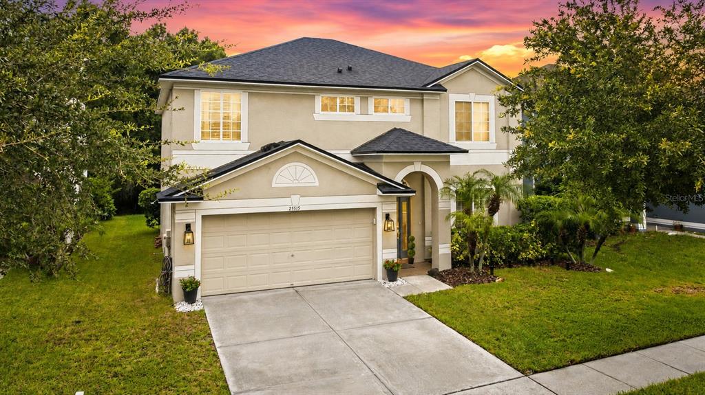 A two-story suburban house with a beige stucco exterior, a two-car garage, and a driveway — 25515 BRUFORD BLVD, LAND O LAKES, FL