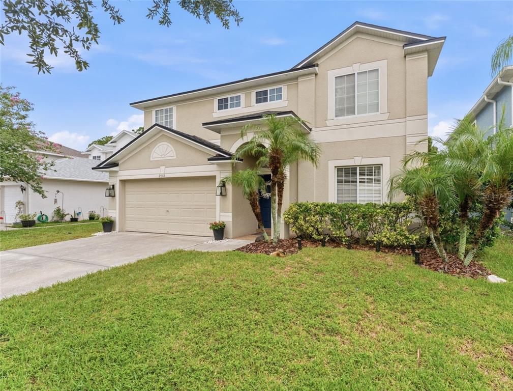 A two-story suburban house with a beige stucco exterior, a garage, and palm trees — 25515 BRUFORD BLVD, LAND O LAKES, FL