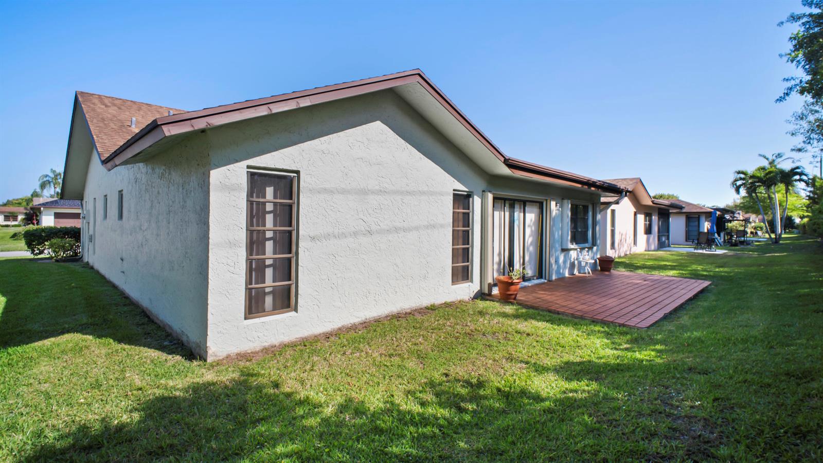 The exterior of a single-story house features a tiled patio and a grassy backyard — 6329 Tall Cypress Circle, FL 33463, FL