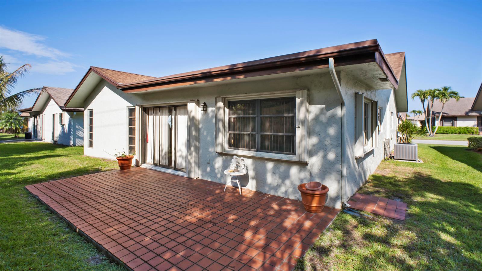 The exterior of a one-story house features a tiled patio, sliding glass doors, and windows — 6329 Tall Cypress Circle, FL 33463, FL