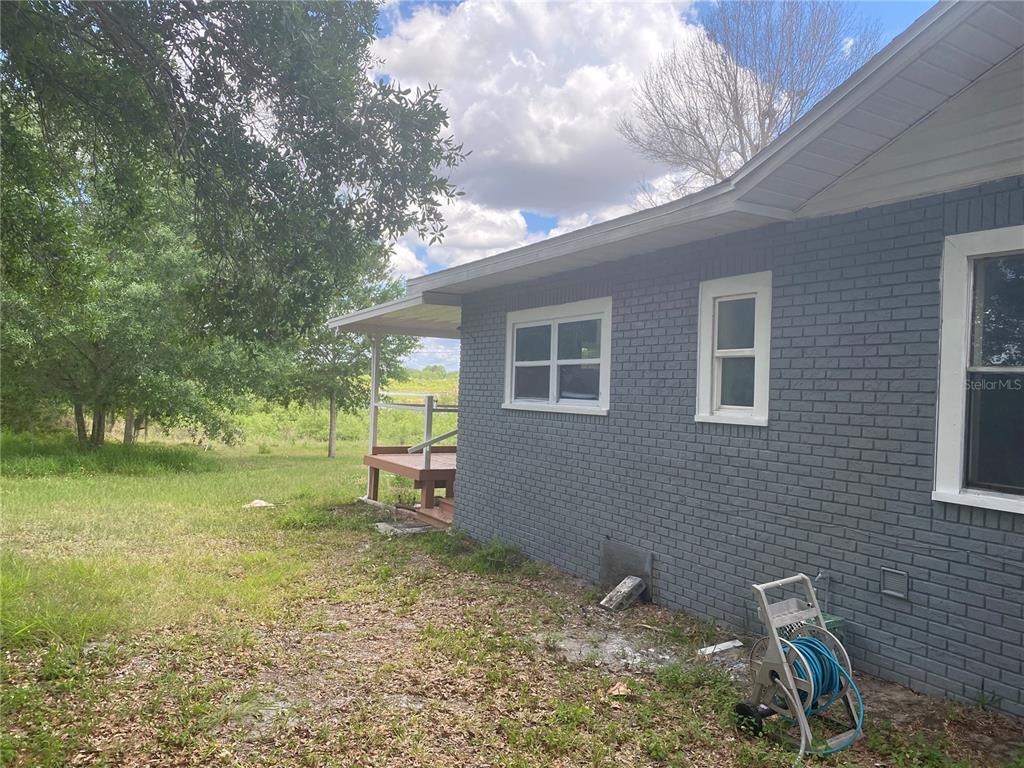A gray brick house exterior features a small wooden deck and a blue garden hose — 431 S MIAMI STREET, LAKE WALES, FL