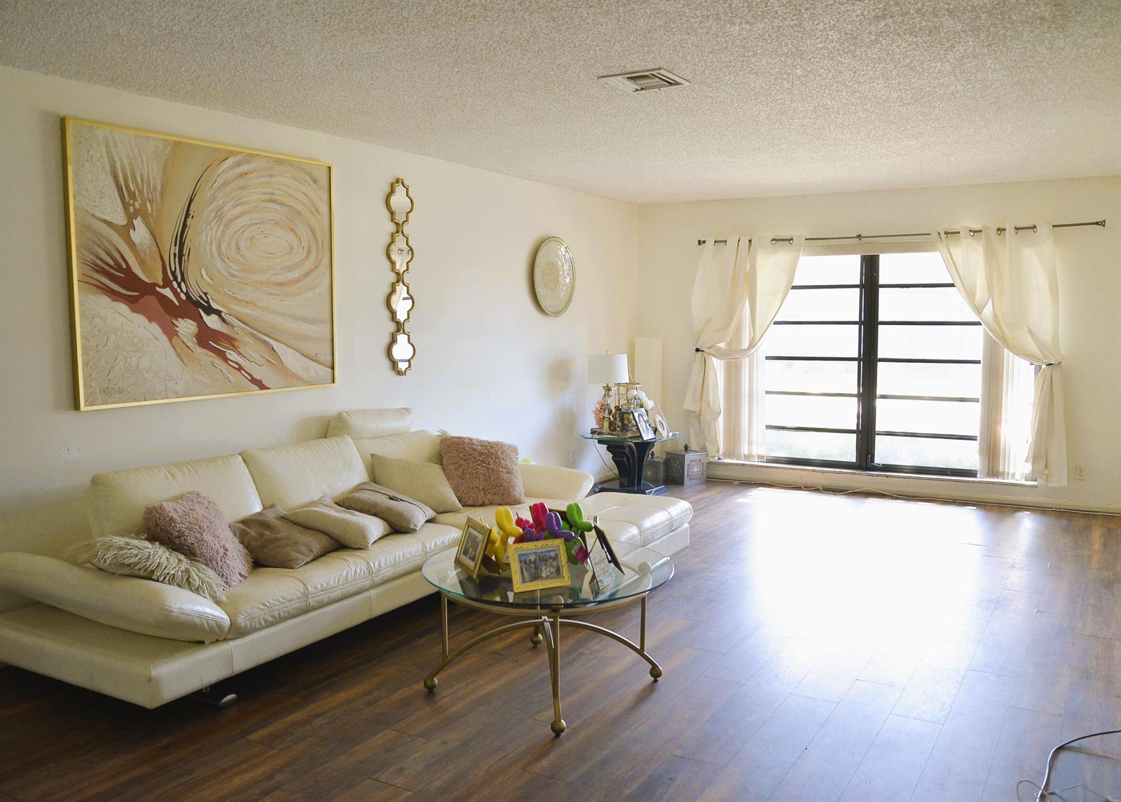 A living room features a white leather sectional, a glass coffee table, and wood flooring — 10054 Eaglewood Road # B, Boynton Beach FL 33436, BOYNTON BEACH, FL