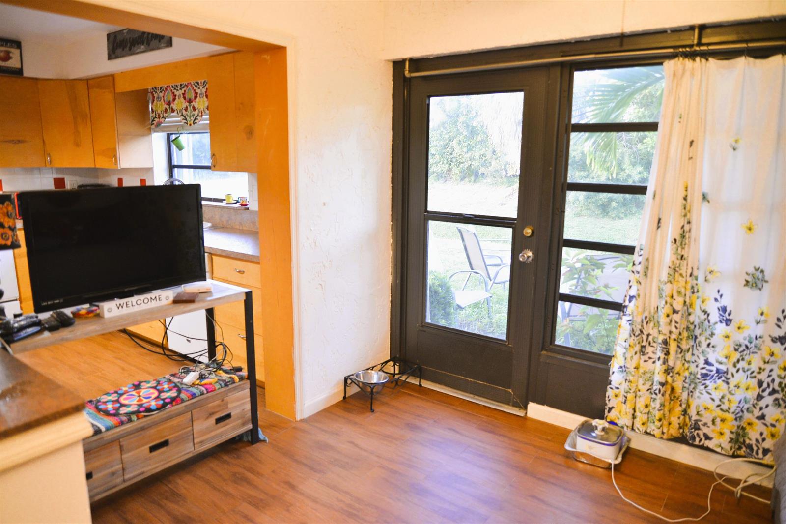 A living area with wood-look flooring connects to a kitchen and a glass-paneled exterior door — 10054 Eaglewood Road # B, Boynton Beach FL 33436, BOYNTON BEACH, FL