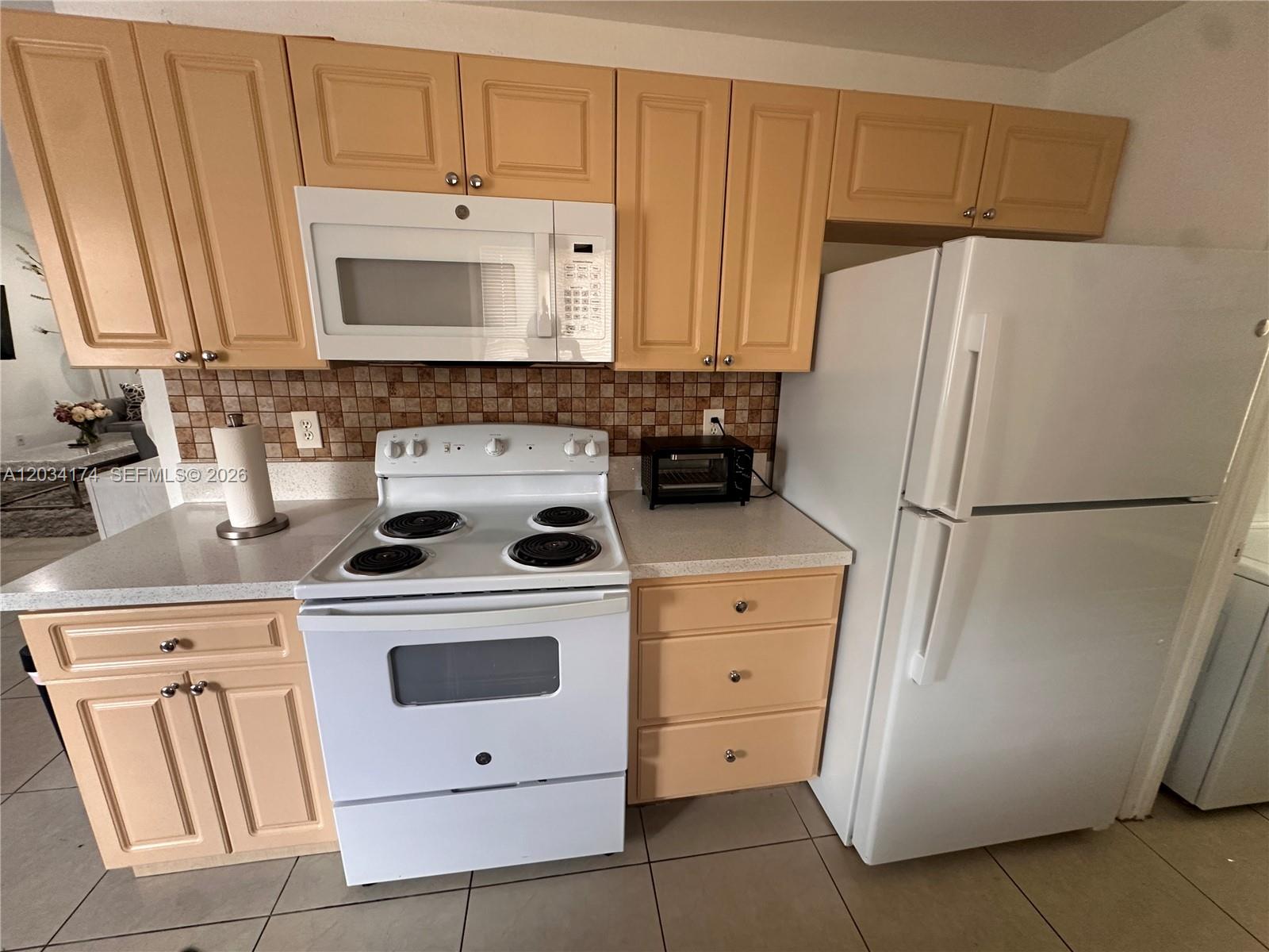 A kitchen features light wood cabinets, white appliances, a tiled backsplash, and light-colored countertops — 404 NW 2nd Ave # A, Hallandale Beach FL 33009, HALLANDALE BEACH, FL