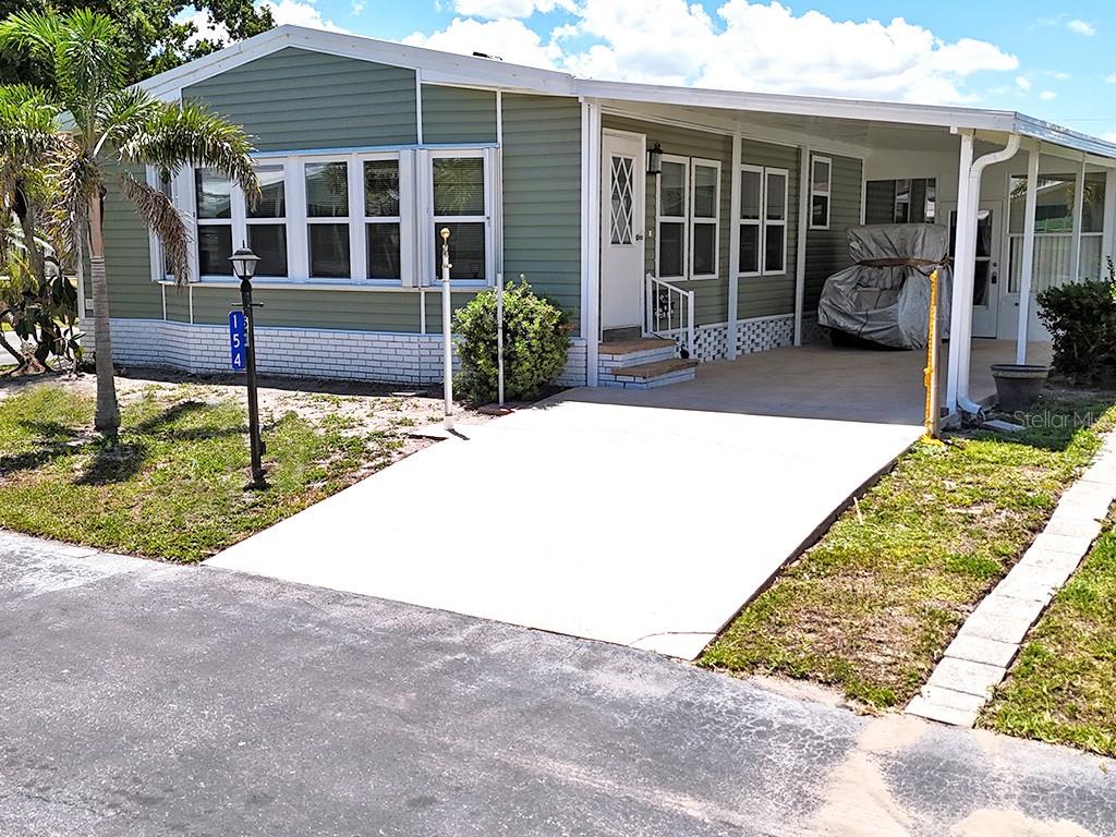 A light green manufactured home features a white brick base, a carport, and a driveway — 15550 BURNT STORE ROAD UNIT 154, PUNTA GORDA, FL