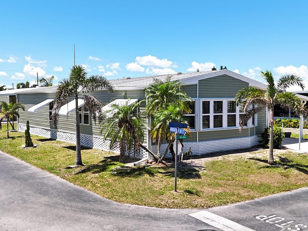 A single-story manufactured home with green siding and white trim sits on a corner lot — 15550 BURNT STORE ROAD UNIT 154, PUNTA GORDA, FL