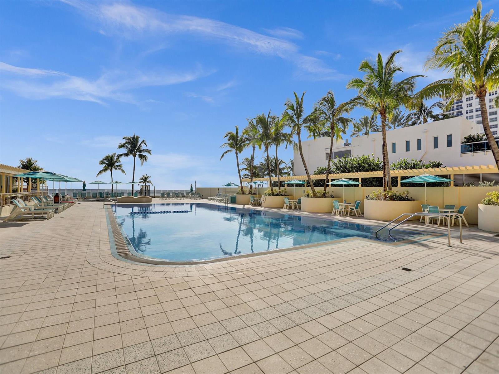 A rectangular outdoor swimming pool surrounded by a tiled deck, palm trees, and patio furniture — 2501 S Ocean Drive # 338, Hollywood FL 33019, HOLLYWOOD, FL
