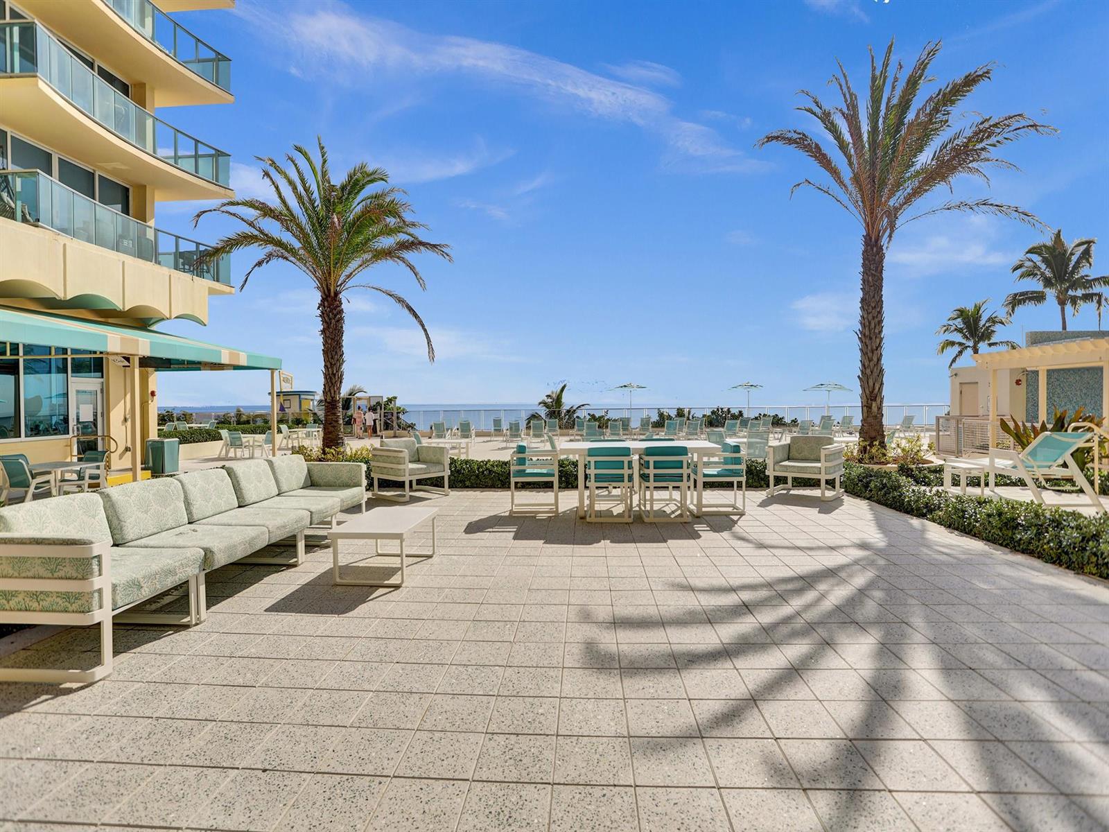An outdoor patio with lounge seating and dining tables overlooks the ocean under a blue sky — 2501 S Ocean Drive # 338, Hollywood FL 33019, HOLLYWOOD, FL