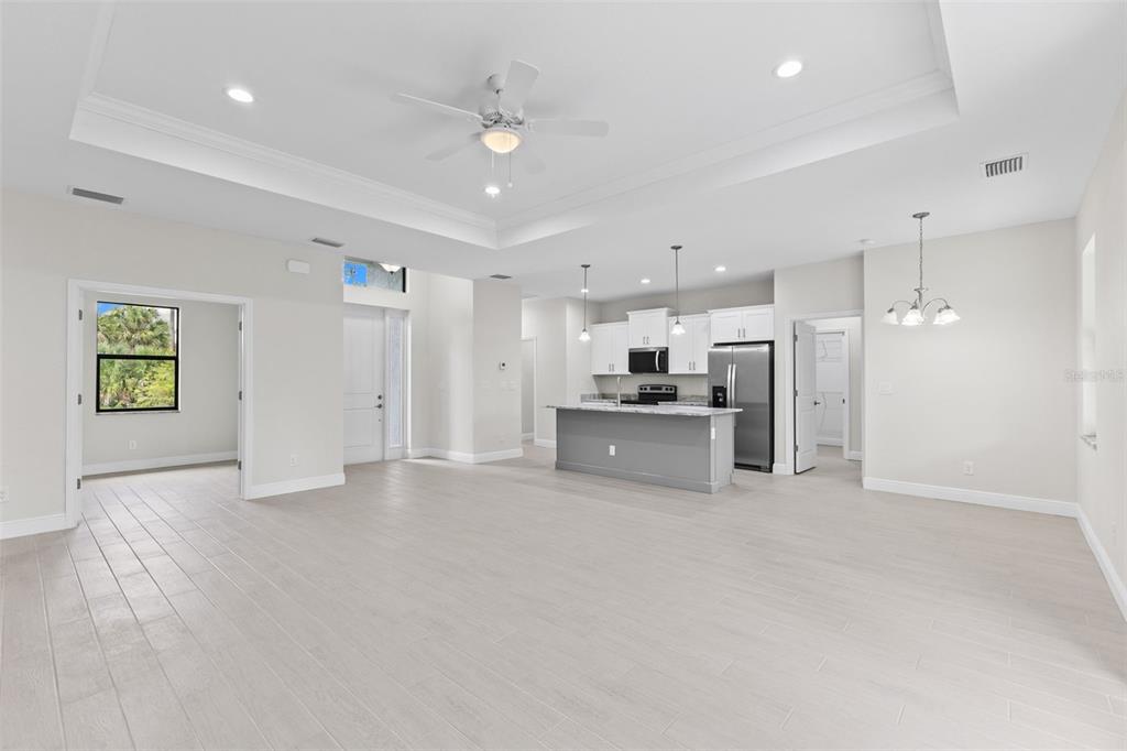 An open-concept living area features light wood-look tile flooring, a tray ceiling, and a kitchen — 2523 WYOLA AVENUE, NORTH PORT, FL