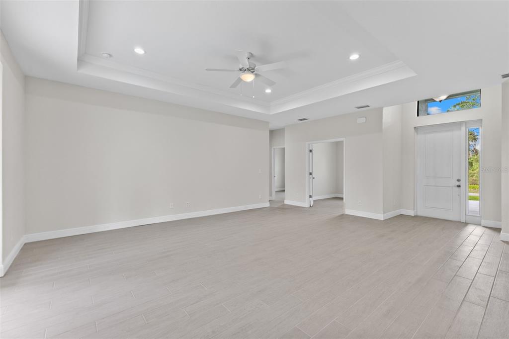 A spacious living room with light-colored tile flooring, a tray ceiling, and a white door — 2523 WYOLA AVENUE, NORTH PORT, FL