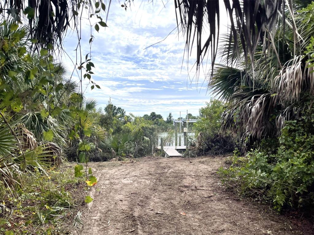 A dirt path leads through dense vegetation toward a small wooden dock on the water — 13281 LONGVILLE AVENUE, PORT CHARLOTTE, FL