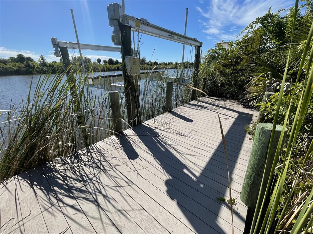 A wooden dock features a boat lift extending over a calm waterway with tall grasses — 13281 LONGVILLE AVENUE, PORT CHARLOTTE, FL