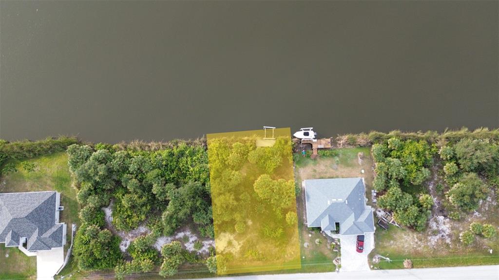 An aerial view shows a vacant, tree-covered waterfront lot situated between two residential homes — 13281 LONGVILLE AVENUE, PORT CHARLOTTE, FL